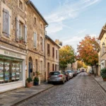 Vue d'une rue typique de la Meuse avec une vitrine d'agence immobilière locale et des bâtiments en pierre traditionnels